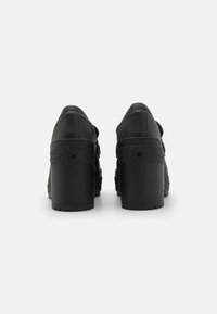 Svarte høye hæler med en glatt lær overdel, teksturerte detaljer, og en kraftig gummisåle med stjernesdesign bak.