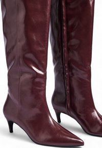 Burgundowe skórzane botki do kolan z ostrym noskiem i niskim obcasem, charakteryzujące się gładką, lekko błyszczącą teksturą oraz bocznym zamkiem.
