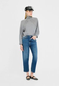 Pilkas ilgomis rankovėmis palaidinė su nėrinių detalėmis, derinama su mėlynais aukštakulniais džinsais. Modelis vilki juodą kepurę ir pilkus lygias batus.