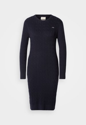 Zila adīta svārku kleita ar kabelu adījuma tekstūru, garām piedurknēm un apaļu kakla izgriezumu. Mazs logotipa elements uz krūtīm.