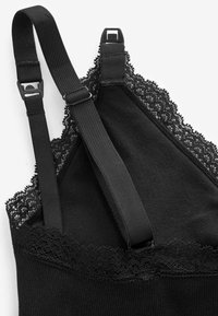 Camisola nera con delicati bordi in pizzo lungo la scollatura, spalline regolabili e morbida trama di tessuto. Design minimalista.