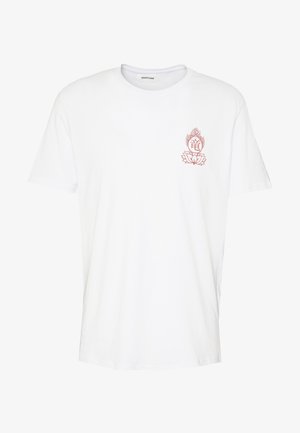 T-shirt en coton blanc avec un petit graphique rouge sur la poitrine, associé à un jean en denim bleu clair et des baskets blanches, mettant en valeur un style décontracté.