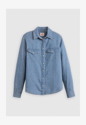 Chemise en denim bleu clair à manches longues, devant à boutons, deux poches poitrine et col pointu. Comprend des boutons en métal argenté et une finition texturée.