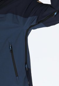 Navy blue waterproof jacket with black accents, featuring zippered pockets and ventilation zips under the arm for breathability.