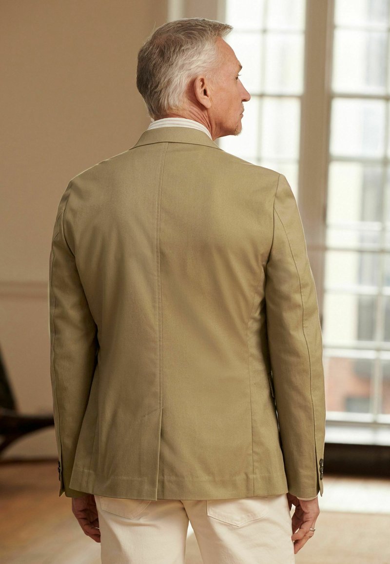 Kaki blazer med et struktureret design, enkelt ventil på bagsiden og to knapper på ærmerne. Bæres over en lys skjorte.