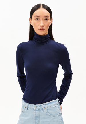 Navyfarbener Rollkragenpullover mit langen Ärmeln aus glattem Stoff, körpernaher Schnitt, mit hohem Kragen und langen Ärmeln, kombiniert mit hellblauen Jeans.