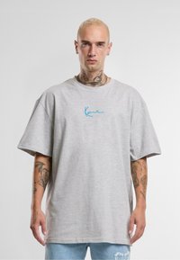 Gray cotton T-shirt with short sleeves and oversized fit. Features blue cursive logo on the chest. Background is plain white.