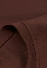 Brązowa bawełniana tkanina o gładkiej fakturze, z przeszytym brzegiem i zakręconym krawędzią, podkreślająca równość materiału.