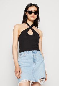 Top preto com decote em buraco de chave, combinado com uma saia de jeans azul claro com bainha desfiada. A modelo usa óculos de sol pretos em formato de gato.