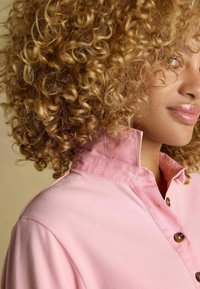 Roosa kaelusega särk, millel on nööpidega kuuldisain, sile puuvillane materjal ja õrnad õmblusteed kaeluse ja nööpide servas.