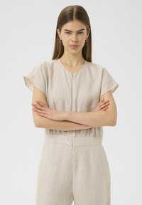 Combinaison en lin beige à manches courtes, décolleté rond et taille froncée. Dotée d'une fermeture éclair à l'avant et d'une texture lisse.