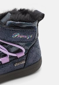 Höga sneakers med en texturerad mörkblå ovandel, svart pälsdetalj, lila snören och en vattentät Gore-Tex-skylt på sidan.