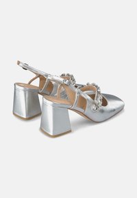 Scarpe con tacco argentate in metallizzato, con punta affusolata, tacco a blocco, cinturino regolabile e decorazioni di strass sul collo del piede.