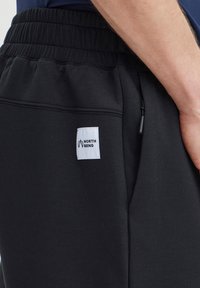 Melnas sporta bikses ar elastīgu vidukli. Ar baltu logo etiķeti ar uzrakstu "NORTH BEND", sānu kabatām un gludu auduma tekstūru.