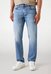 Lichtblauwe jeans met een rechte pasvorm, voorzien van whiskerpatronen, vijf zakken en een knoopsluiting, gedragen met witte sneakers.