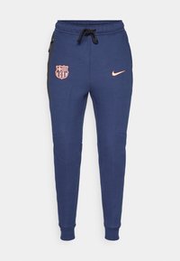 Navy blue sweatpants with elastic cuffs, featuring a pink logo and Barcelona shield, side pockets, and black side panel accents.