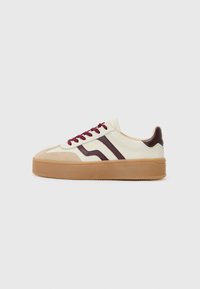 Sneaker med en kremfarget overdel, maroon detaljer, teksturert beige semsket skinn, og en tykk gummisåle. Har maroon snøringer og to parallelle striper.