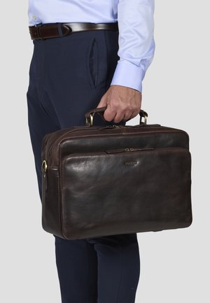 Malette en cuir marron avec deux poignées supérieures, fermeture éclair et quincaillerie dorée. Texture lisse, forme rectangulaire et détail du logo embossé.