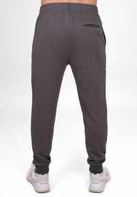 Jogging gris avec une coupe décontractée, taille élastique, poche arrière et poignets fuselés, assortis à des baskets blanches.