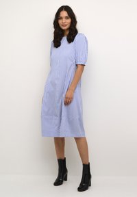Kék és fehér csíkos midi ruha rövid puffos ujjakkal, kerek nyakkivágással és fodros aljjal. Fekete bokacsizmával párosítva.