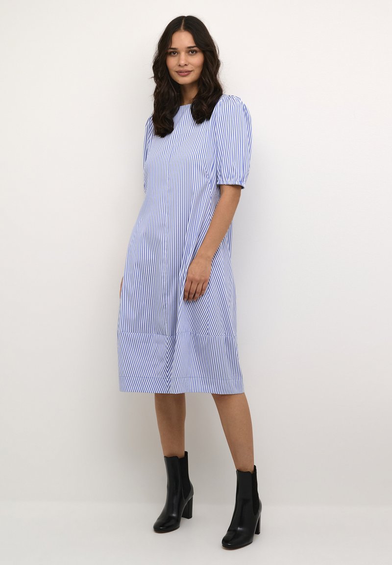 Kék és fehér csíkos midi ruha rövid puffos ujjakkal, kerek nyakkivágással és fodros aljjal. Fekete bokacsizmával párosítva.