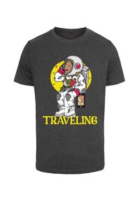 Mørkegrå t-shirt med et astronautmotiv med en gul cirkel baggrund; teksten "TRAVELING" i fed gul nedenunder, legende designelementer.