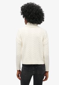 Crème kabelgebreide trui met hoge kraag, geribde manchetten en tailleband; heeft een textuurpatroon en een cropped silhouet.