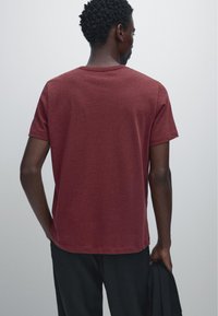 Bordeauxfarbener Baumwoll-T-Shirt mit kurzen Ärmeln, Rundhalsausschnitt und lässigem Schnitt. Glatte Textur, gerader Saum, von hinten betrachtet.