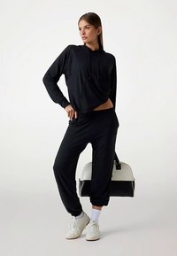 Hanorac negru cu croială lejeră și șnur reglabil, asortat cu pantaloni de jogging de aceeași culoare. Completat cu adidași albi și o geantă în contrast.