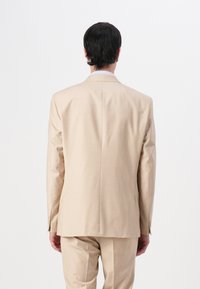 Beige Blazer aus glattem Stoff, mit einem einzelnen Schlitz, schlanker Passform und minimalen Nähdetails. Die Rückansicht zeigt klare Linien.