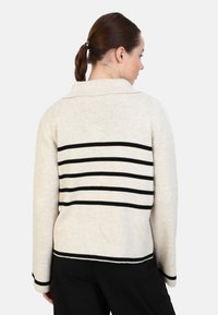 Maglione crema con strisce orizzontali nere sul retro. Presenta un colletto e maniche lunghe, realizzato in un morbido materiale a maglia.