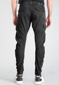 Los pantalones cargo negros presentan un corte ajustado, múltiples bolsillos y una tela texturizada. Se llevan con zapatillas blancas y negras.