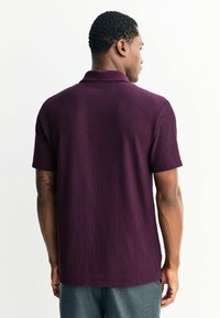 Poloko s krátkym rukávom v tmavo fialovej farbe, rebrovaná textúra, klasický golier, pohľad zospodu, s jemným lemom a bez viditeľných log a vzorov.