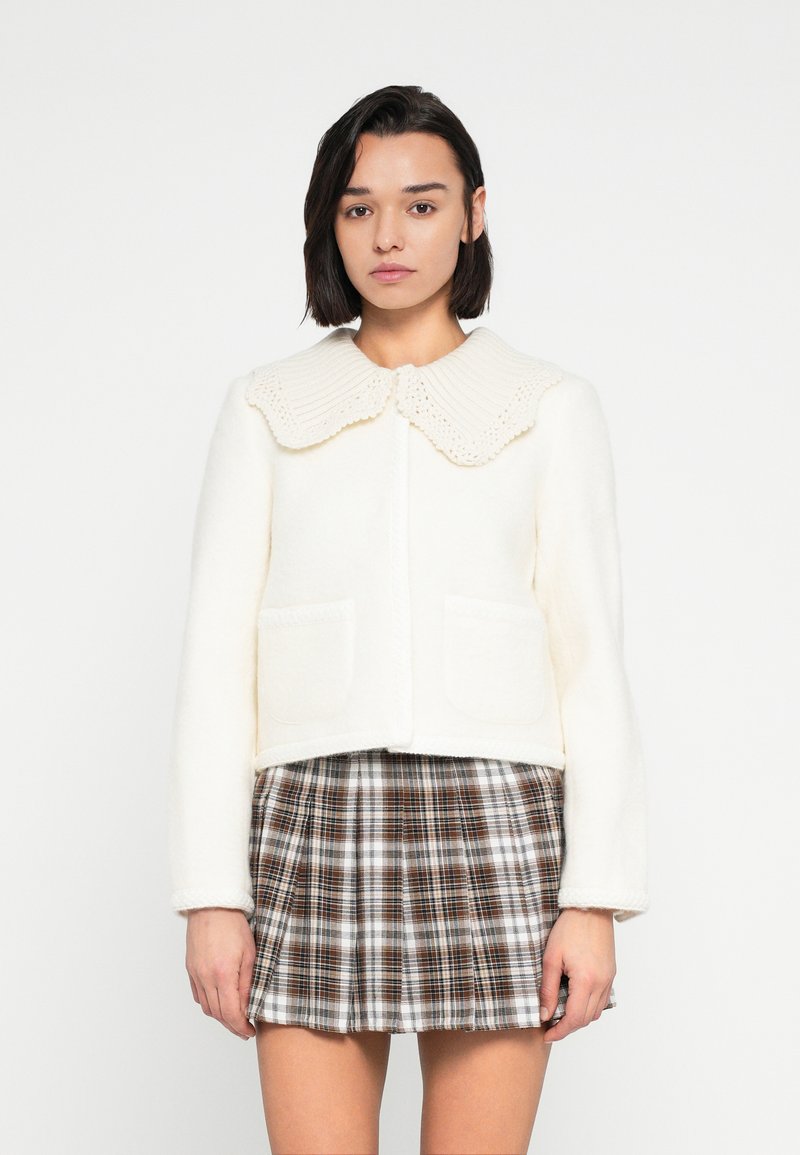 Λευκό σακάκι από μείγμα μαλλιού με ριμπ πλεκτό, κυματιστό γιακά και δύο μπροστινές τσέπες, σε συνδυασμό με καφέ καρό πλισέ φούστα.