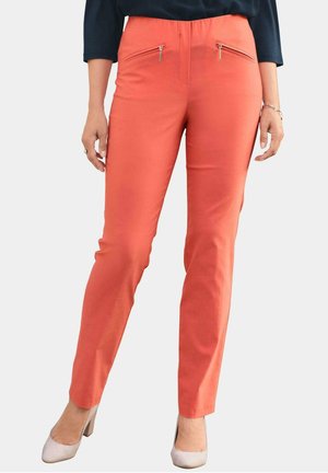 Pantalons couleur corail à coupe slim, dotés de deux poches zippées à l'avant et d'une texture lisse, assortis à des chaussures de couleur claire.