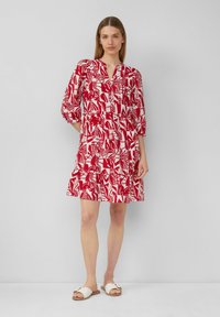Rot-weißer, blumengemusterter Kleid mit geknöpftem Ausschnitt, DreiviertelÄrmeln und einem gestuften Rock, kombiniert mit weißen Slipper-Sandalen.