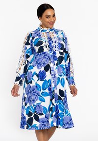 Bloemig jurkje met blauw en wit kleuren, ingewikkelde kantafwerking op de mouwen, knopen aan de voorkant en een knie-lange snit met een ontspannen pasvorm.