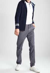 Marinblå hoodie med ränder på muddarna, vit pikétröja med krage, grå byxor och vita sneakers. Avslappnad outfit med ett lager-på-lager utseende.