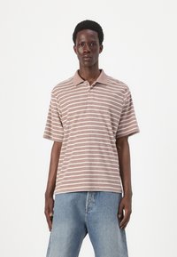 Kortærmet polo-shirt i brun med hvide striber, med en kontrastfarvet krave og tre knapper, parret med lyseblå denimjeans.