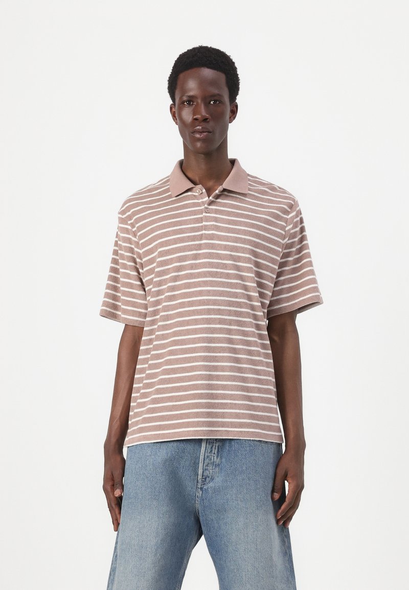 Kortærmet polo-shirt i brun med hvide striber, med en kontrastfarvet krave og tre knapper, parret med lyseblå denimjeans.