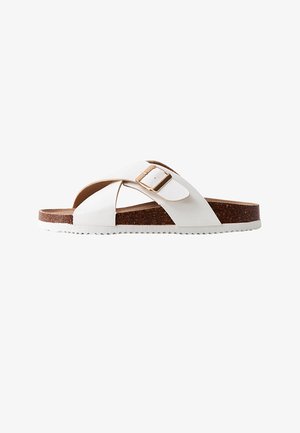 White slide sandal with brown cork sole, wide crisscross straps, and a gold buckle on a white background.