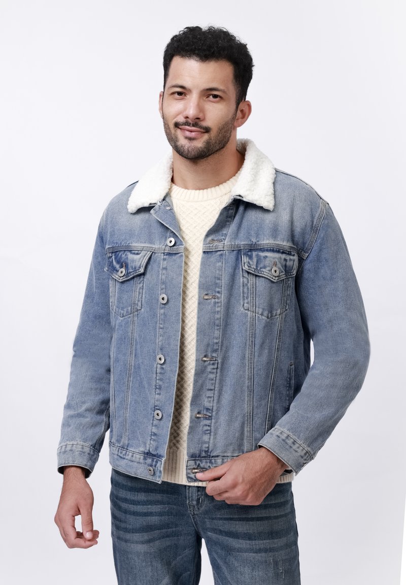 Lichtblauwe denim jas met een nepbont kraag, knoopsluiting en twee borstzakken. Draagt over een crèmekleurige trui.