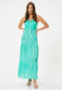 Lang, turkis satin kjole med lagdelt bund, justerbare spaghetti stropper og en samlet brystdel. Båret med hvide flip-flops.