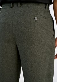 Ciemnozielone spodnie wykonane z teksturowanej tkaniny, z tylną kieszenią z detalem w postaci guzika. Fason jest dopasowany, z gładkim wykończeniem.