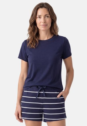 Femme portant un haut bleu marine à manches courtes et un short bleu marine avec des rayures blanches horizontales et une taille à cordon, debout avec une main dans la poche.