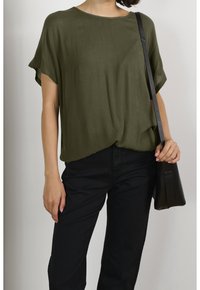 Top di un verde oliva, morbido e dalla vestibilità ampia, realizzato in un tessuto texturizzato. Abbinato a pantaloni neri e a una piccola borsa a tracolla nera.