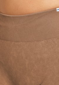 Fascetta a coste marrone dei leggings, con una texture morbida e materiale liscio. Il tessuto appare leggermente testurizzato sotto la fascetta.