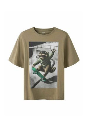 T-shirt marron avec un graphisme d'un raton laveur portant des lunettes de soleil et un sweat à capuche, roulant sur un skateboard vert dans un skatepark.