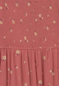 Kleid in Korallenfarbe mit Blumenmuster, gerafftem Oberteil und eingesetztem Rock. Der Stoff wirkt leicht und weich.