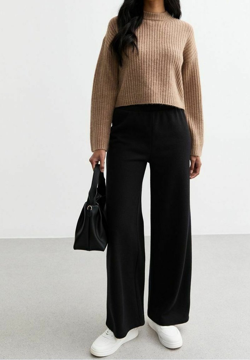 Pull en maille côtelée marron, pantalon large noir, baskets blanches et petit sac à main noir. Matières texturées et coupe décontractée.